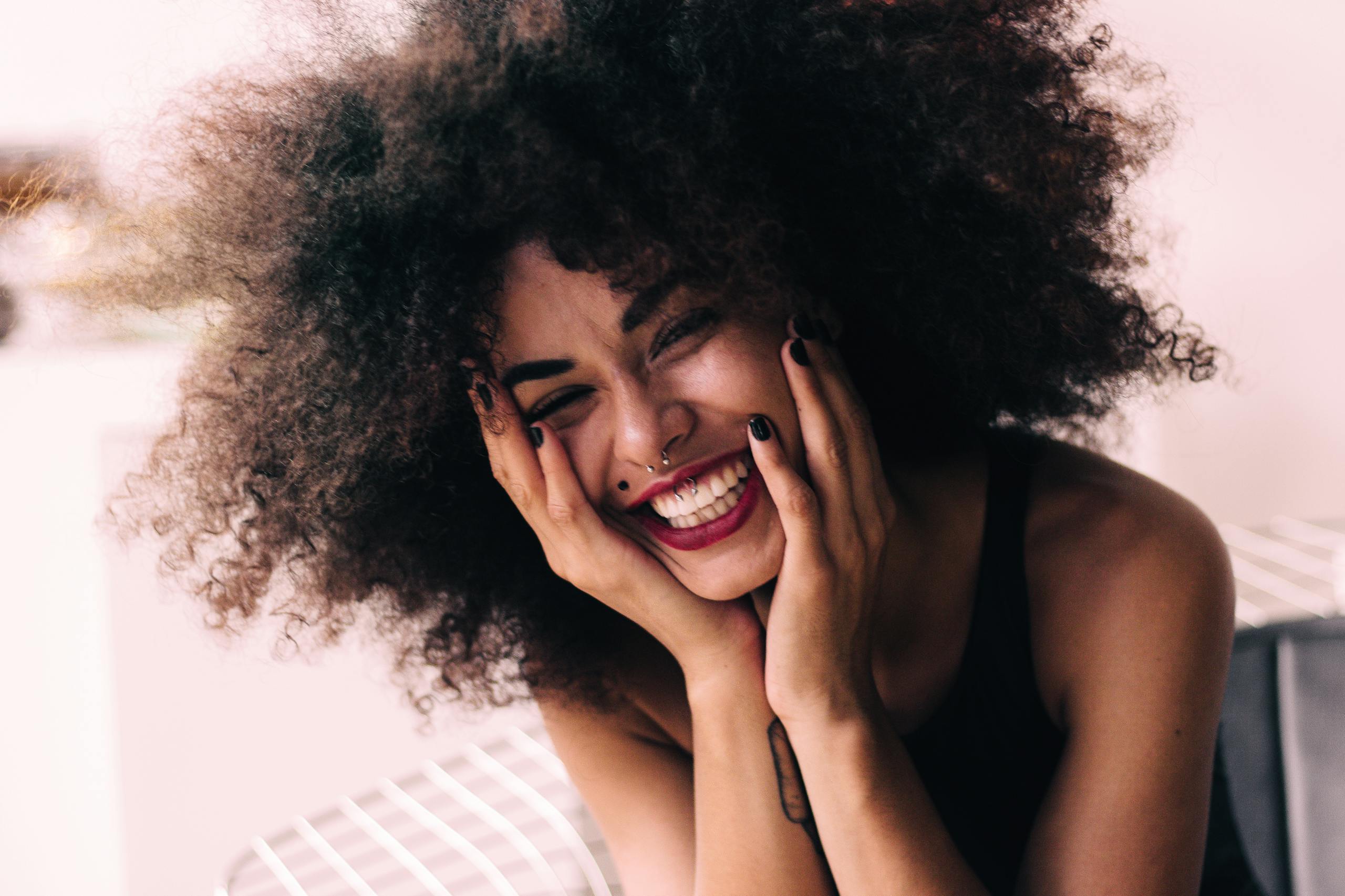 Close-up of a happy woman with curly hair smiling joyfully indoors.